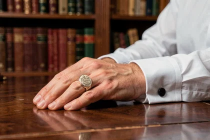 Chevalière en or blanc sur la main d'un homme élégant posée sur un bureau en acajou, gravée d'un blason familial